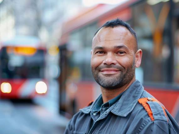 A smiling man in work clothes with a bus behind him