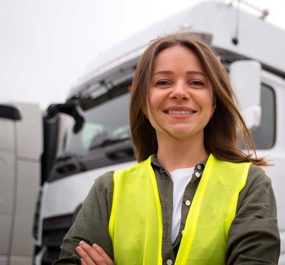 A smiling woman in a high-visibility vest in front of a lorry