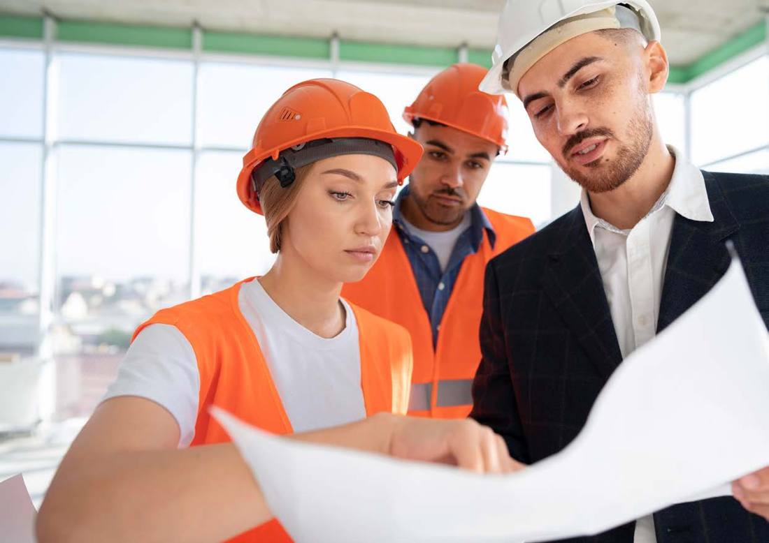 Three colleagues in hard hats looking at plans