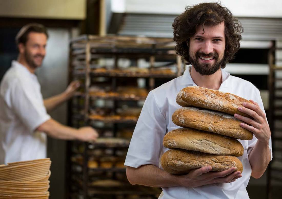 A baker holding loaves in a busy kitchen