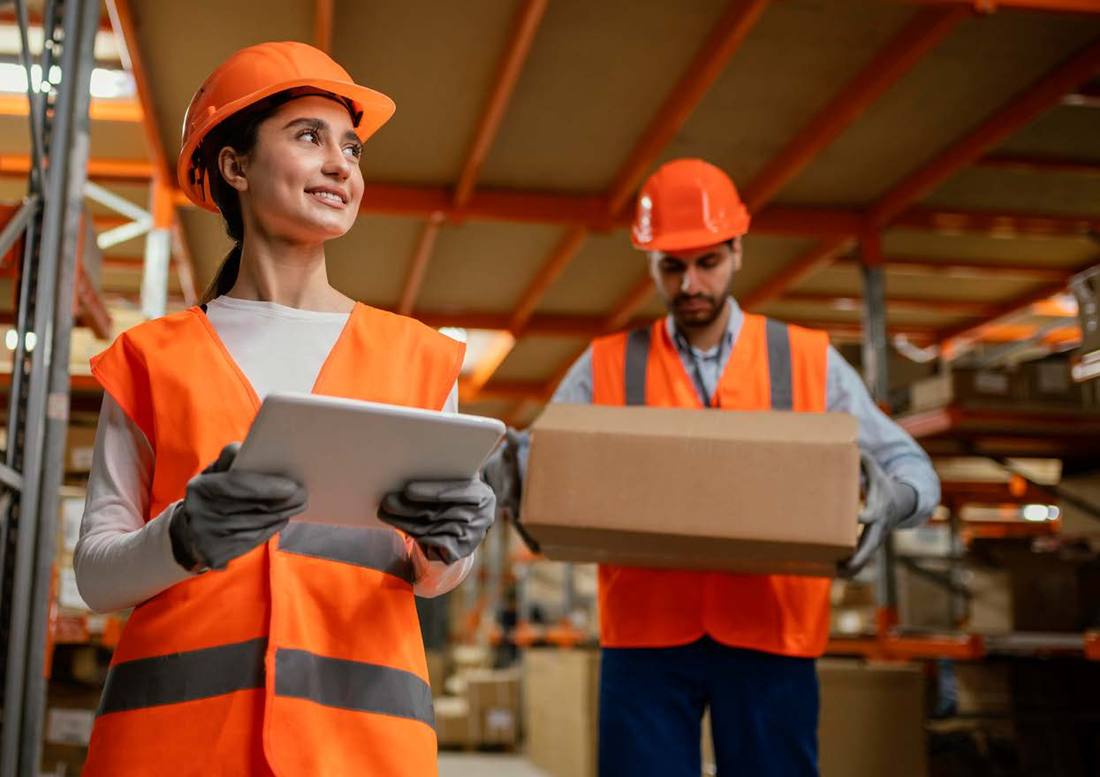 Two warehouse colleagues, one holding a box and the other a tablet